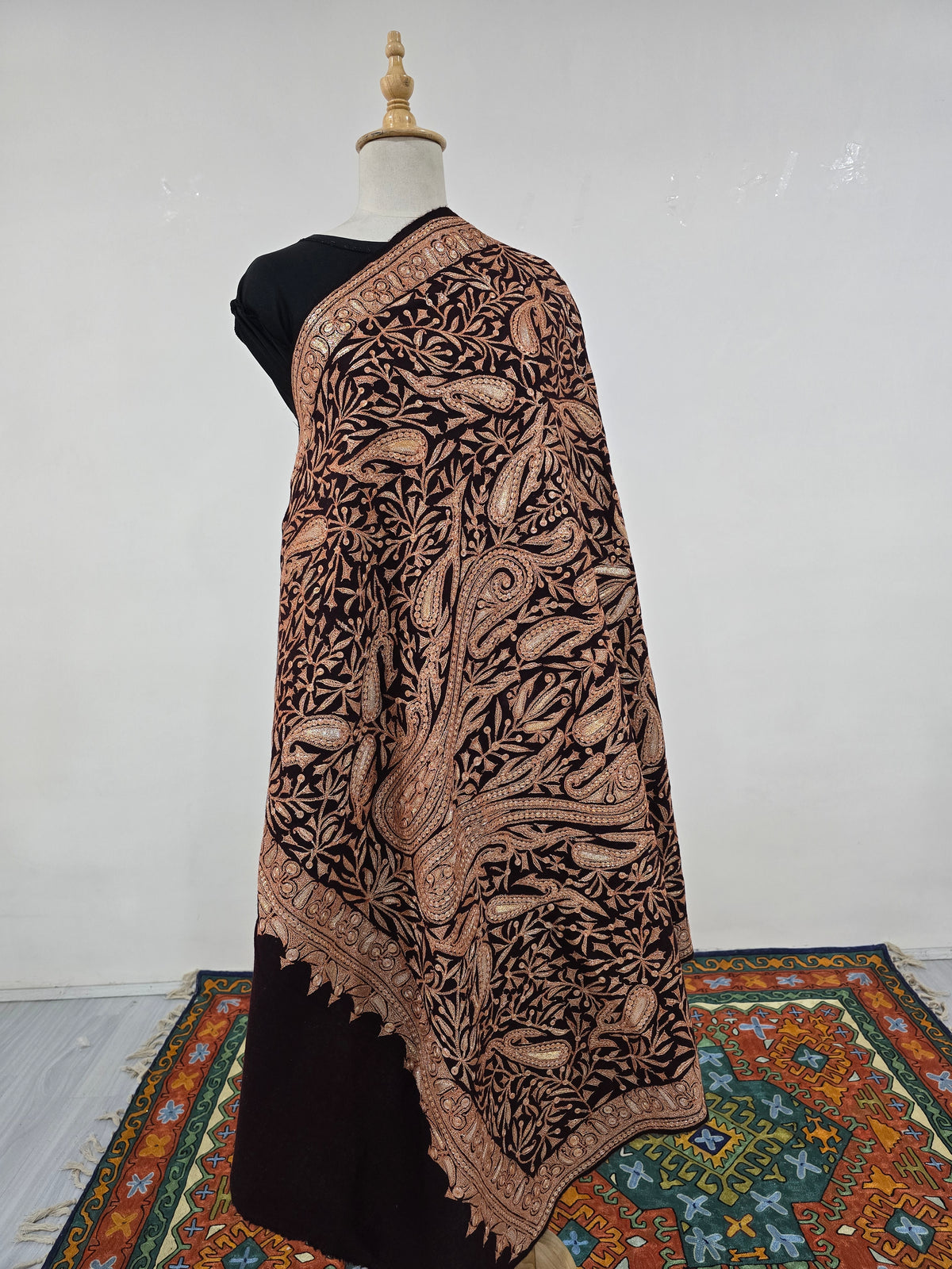 Full draped view of the dark brown merino wool shawl, densely embroidered with copper-gold paisleys and leafy vines.