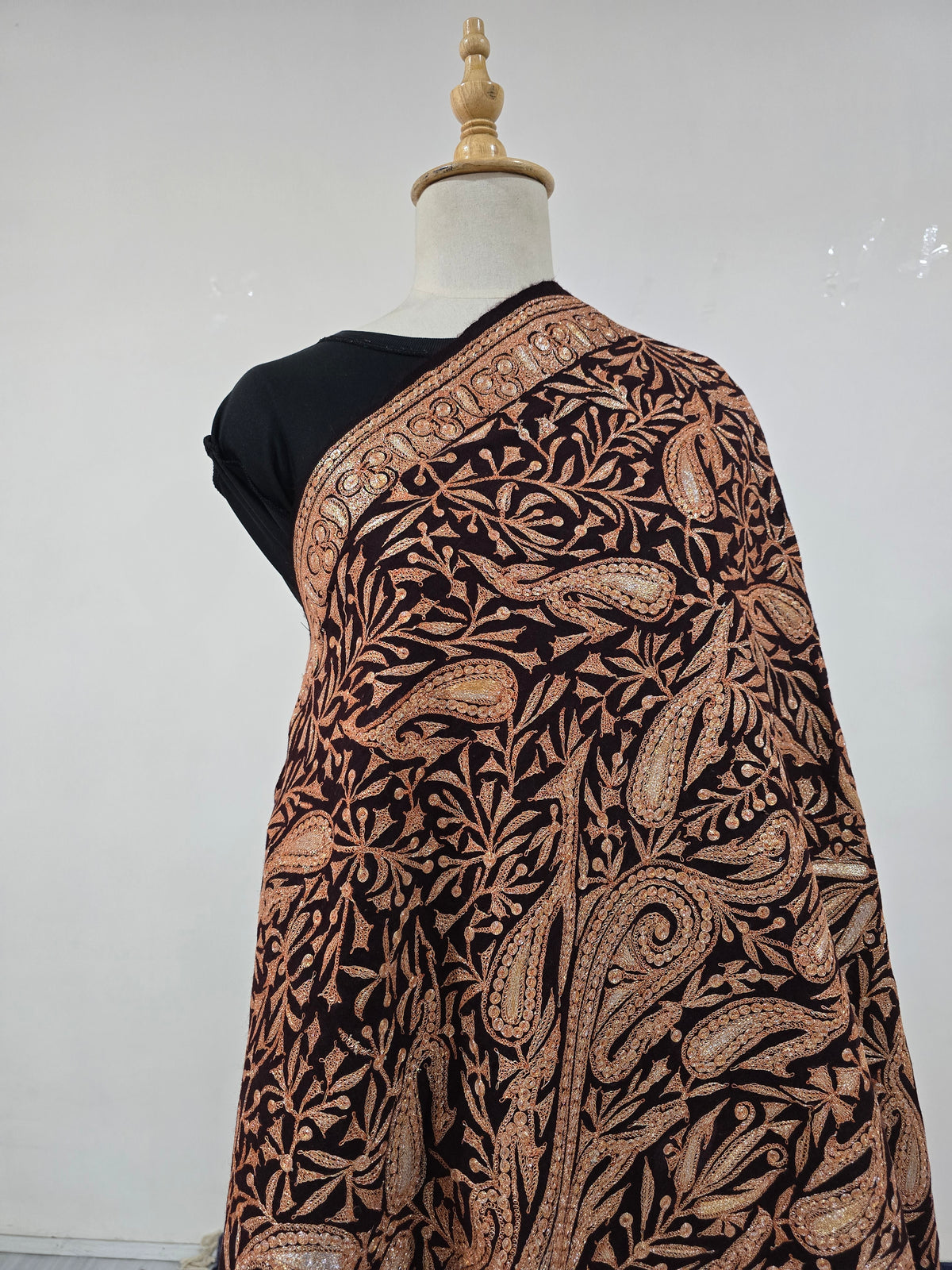Upper view of the shawl across a mannequin shoulder, showing large copper-gold paisleys beneath a narrow patterned border.