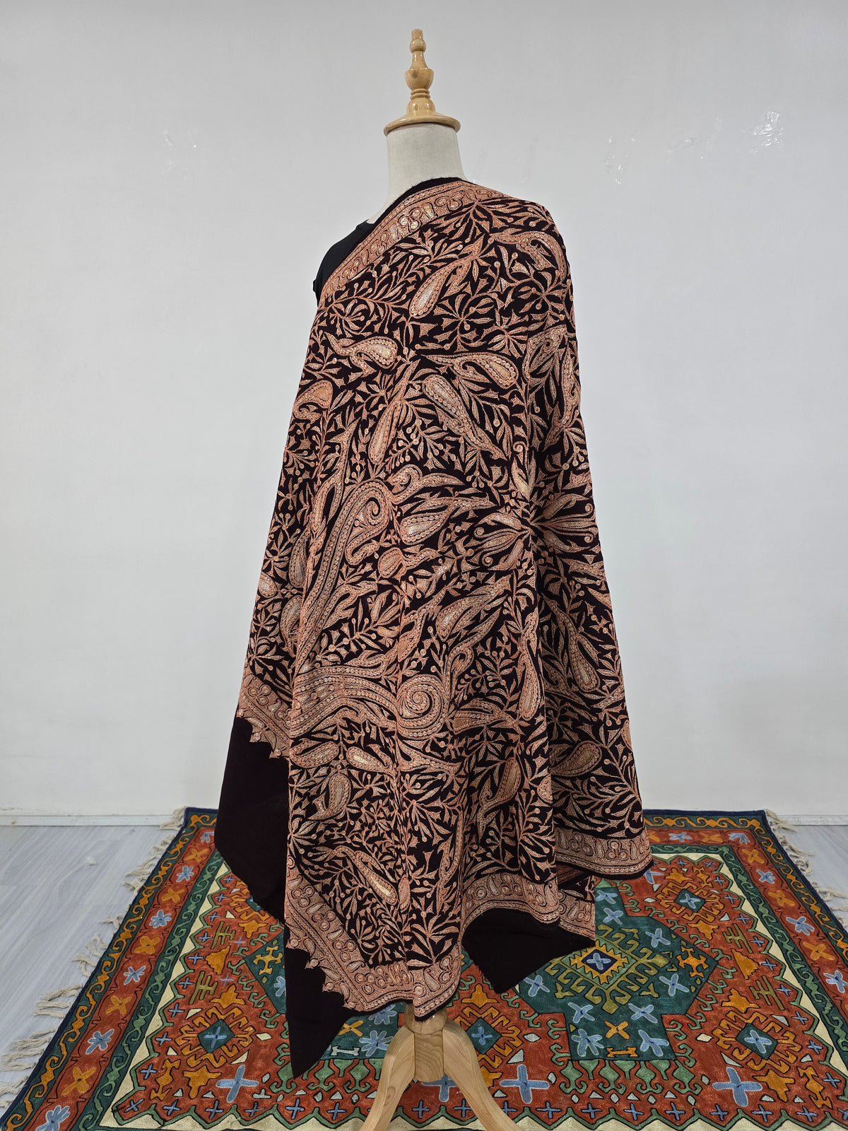 Angled full view of the embroidered brown shawl with flowing paisleys, a scalloped border and plain dark ends.