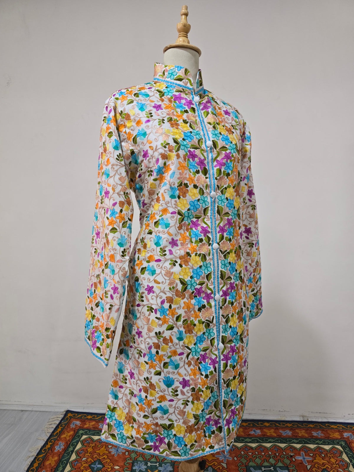 Angled full view of the white floral jacket, showing its long silhouette, covered-button front and blue-trimmed hem.