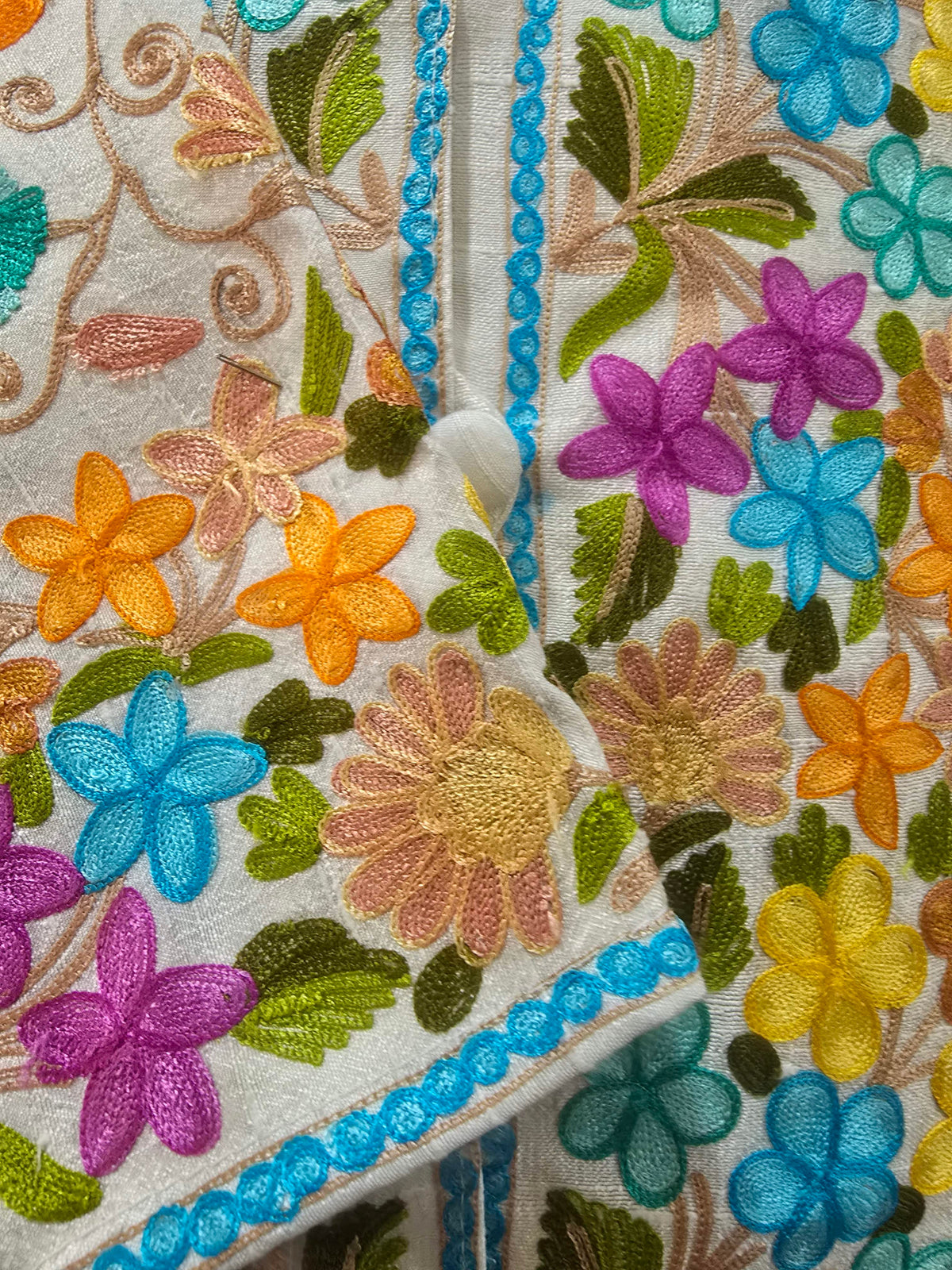 Close-up of the jacket cuff crossed over the front, showing bright floral embroidery, blue edging and a white covered button.