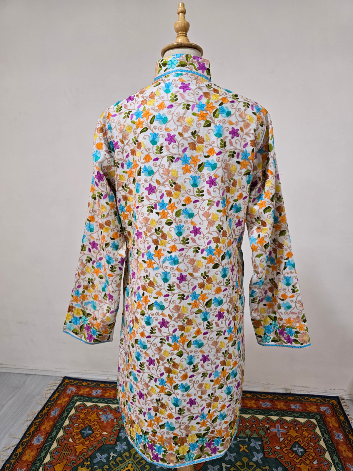 Full back view of the white long jacket with all-over colourful flowers, a stand collar and blue-trimmed cuffs and hem.