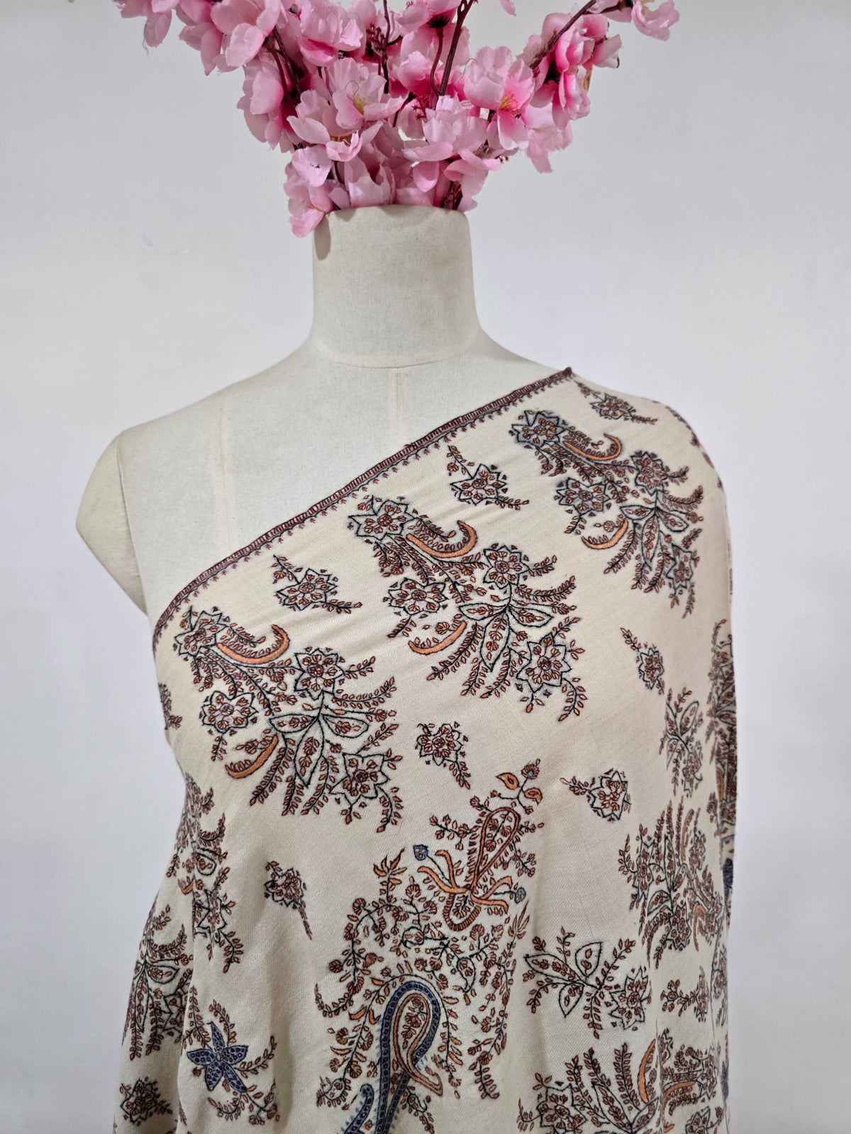 Upper drape of a cream Pashmina shawl showing brown leafy embroidery, blue paisley accents and a narrow embroidered edge