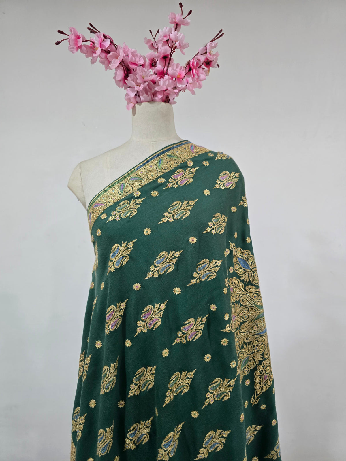 Emerald-green Pashmina shawl draped on a mannequin, with gold motifs accented in blue and lilac and an ornate border