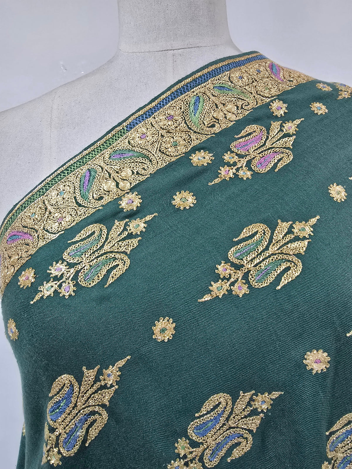Shoulder close-up of emerald-green Pashmina shawl showing gold embroidery with blue and lilac accents beside the border