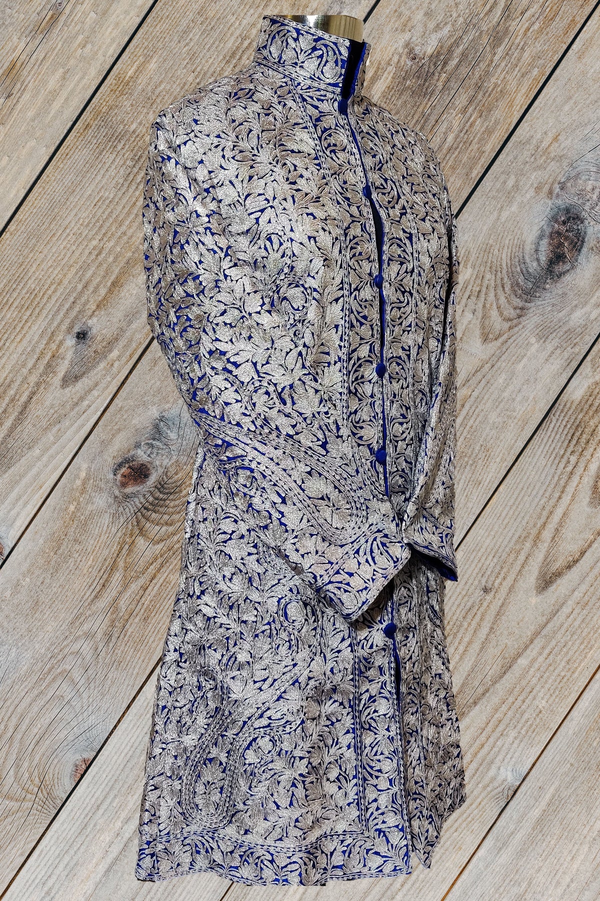 Front of the deep blue Aari jacket with sleeves crossed inward, showing matching silver-toned floral cuffs and dense embroidery.