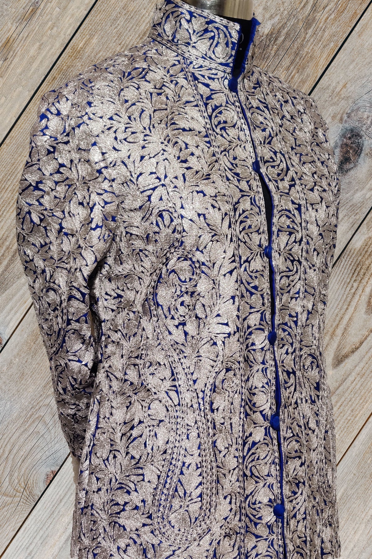 Closer angled view of the jacket’s high collar and chest, densely covered in silver-toned Aari flowers over deep blue fabric.