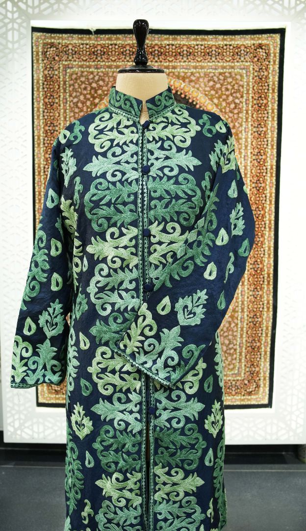 Full front of the navy jacket on a mannequin, showing green leaf embroidery, a stand collar and one crossed sleeve