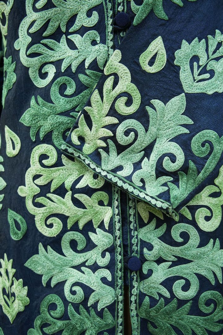 Crossed cuff of the navy jacket with green Aari leaves, curled stems and small teardrop motifs