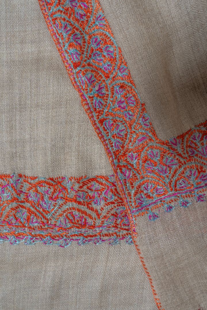 Folded corner of the beige shawl showing overlapping multicoloured floral borders and reverse stitching