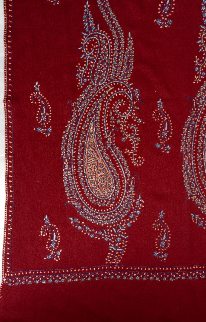 Close-up of a large blue, pink and gold Sozni paisley medallion beside small motifs on deep red fabric
