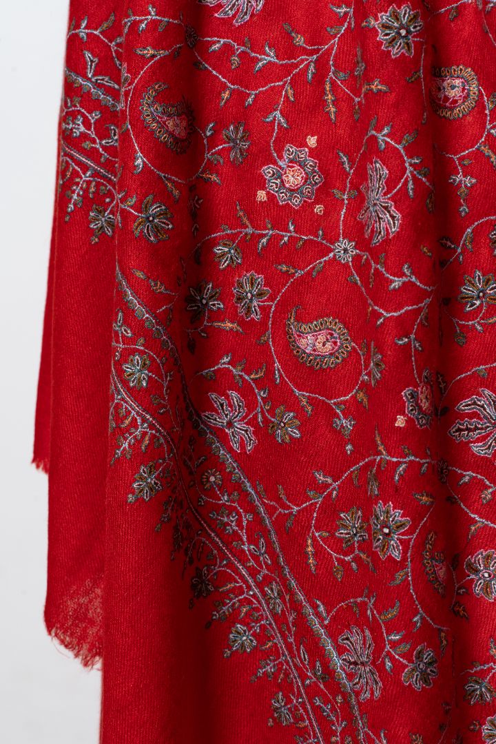 Hanging scarlet shawl folds showing pale Sozni paisleys, flowers and leafy vines beside a plain fringed end