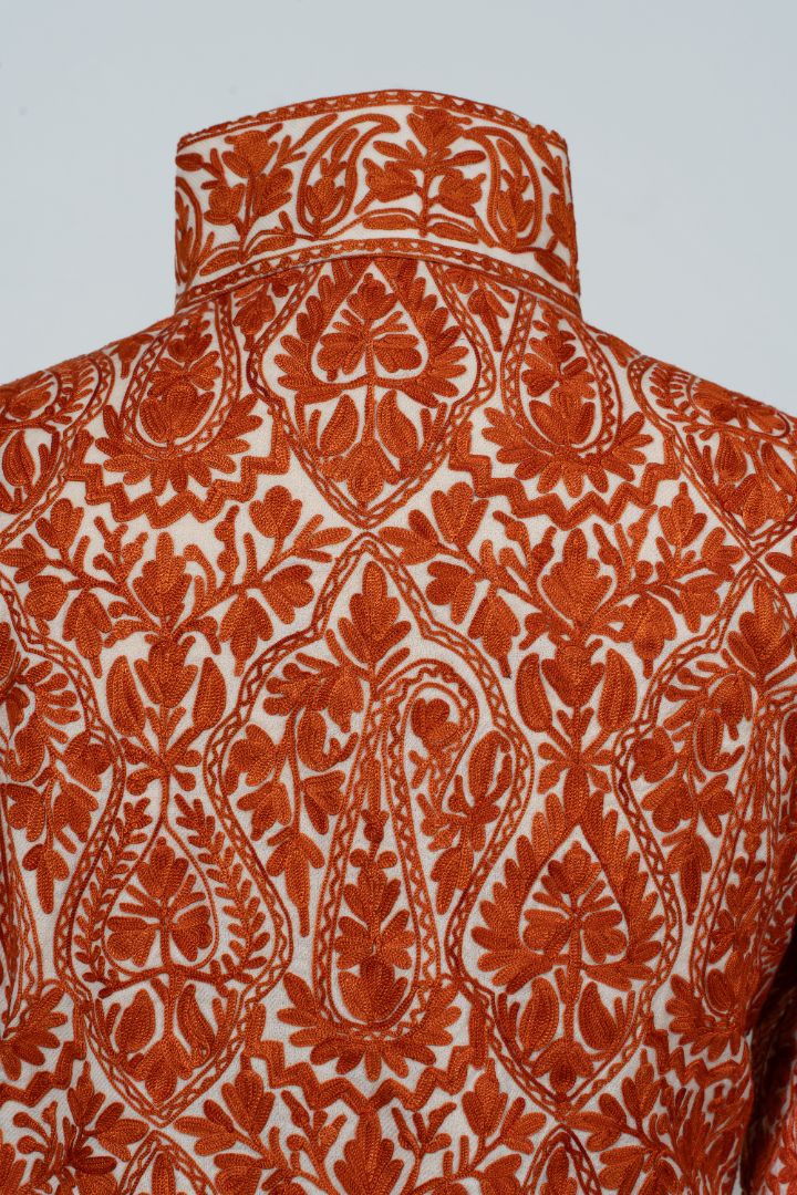 Upper back close-up of the jacket with dense orange paisley and leaf motifs beneath the embroidered stand collar.