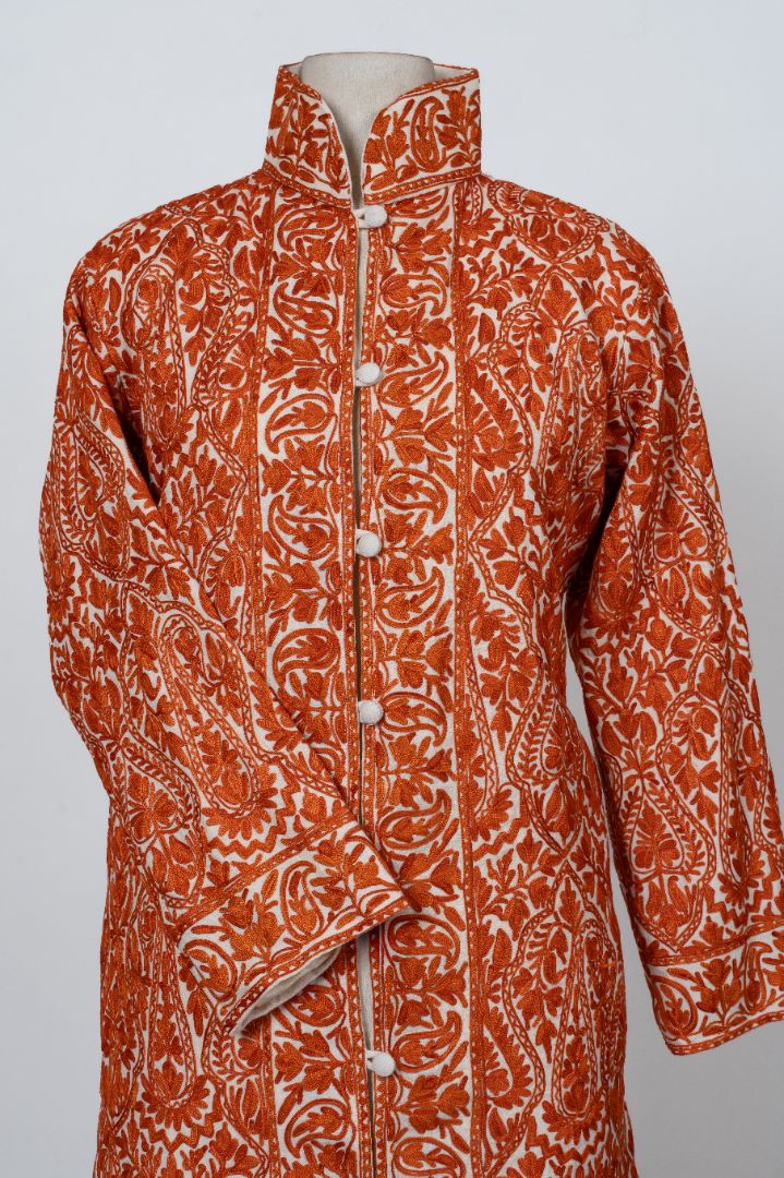 Front view of the saffron embroidered jacket with a stand collar, white covered buttons and one sleeve crossed.