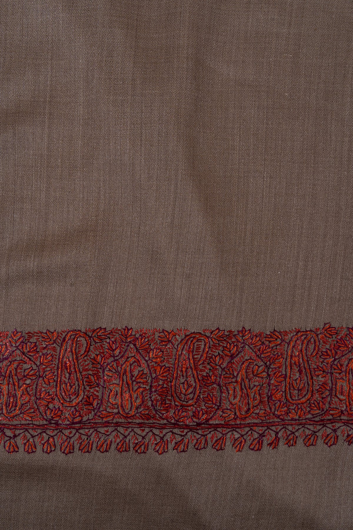 Close-up of the rust Sozni paisley border and hanging leaf motifs on mocha-brown wool