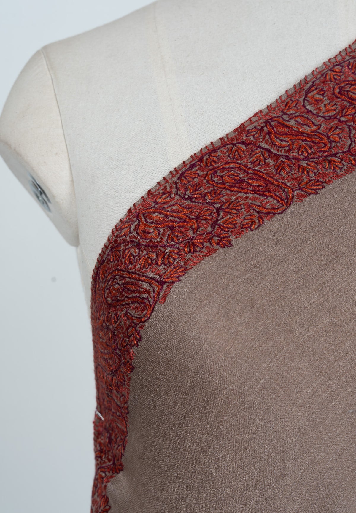 Close-up of rust paisley and leaf embroidery along the mocha shawl's shoulder edge