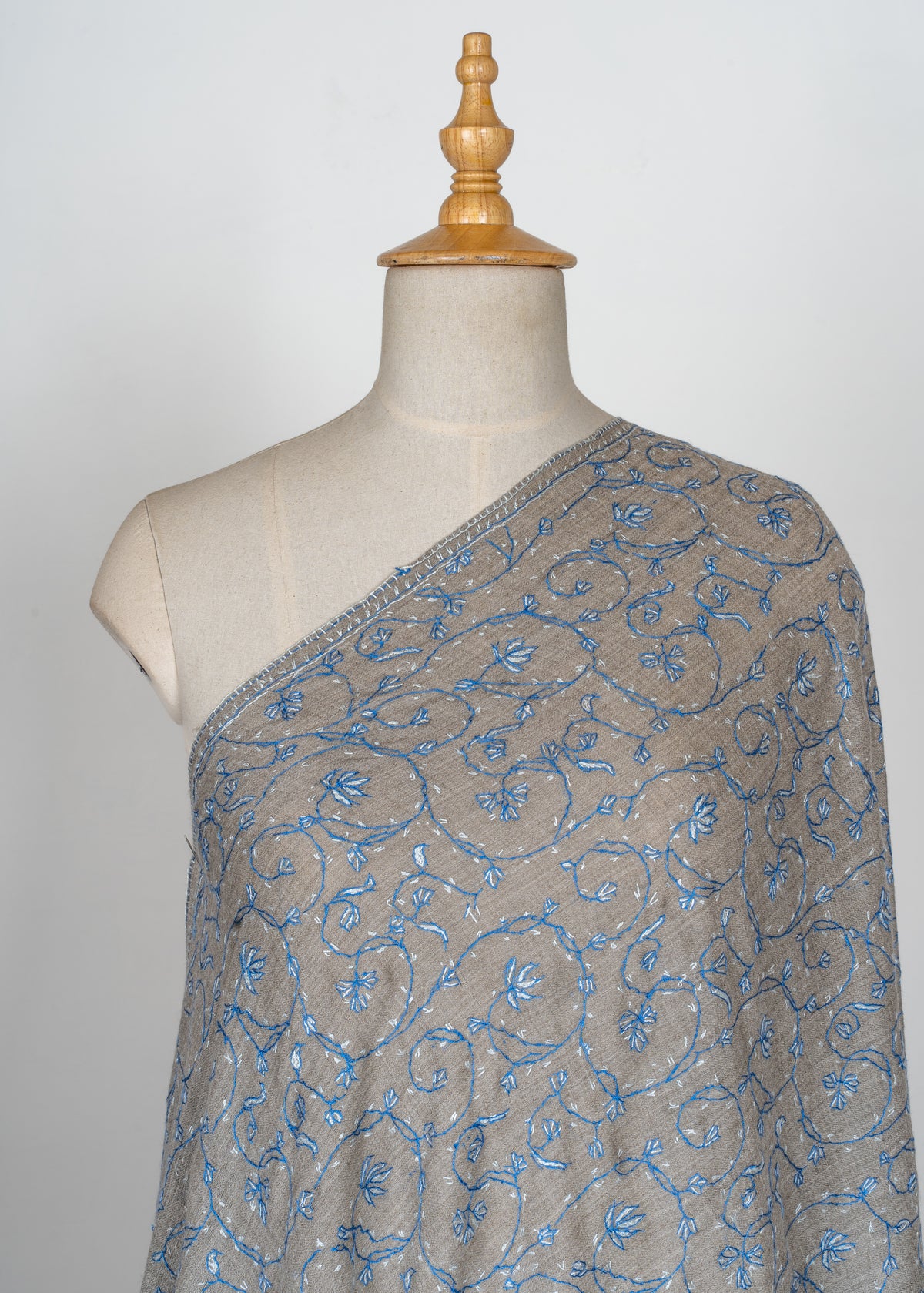 Dove-grey shawl draped over a mannequin with sky-blue and pale Sozni floral vines flowing across the fabric