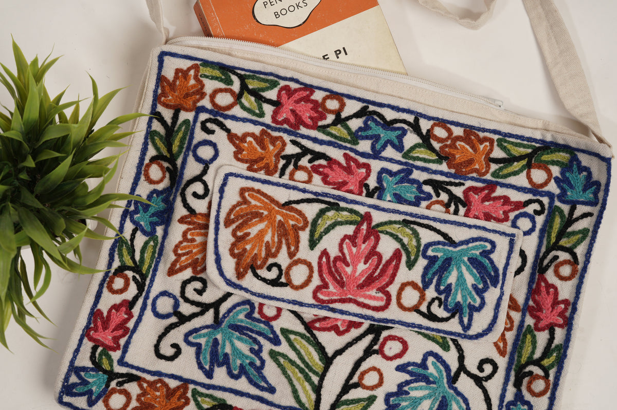 Close-up of a cream cotton bag with a zip top and red, blue and orange Aari leaf motifs outlined in navy