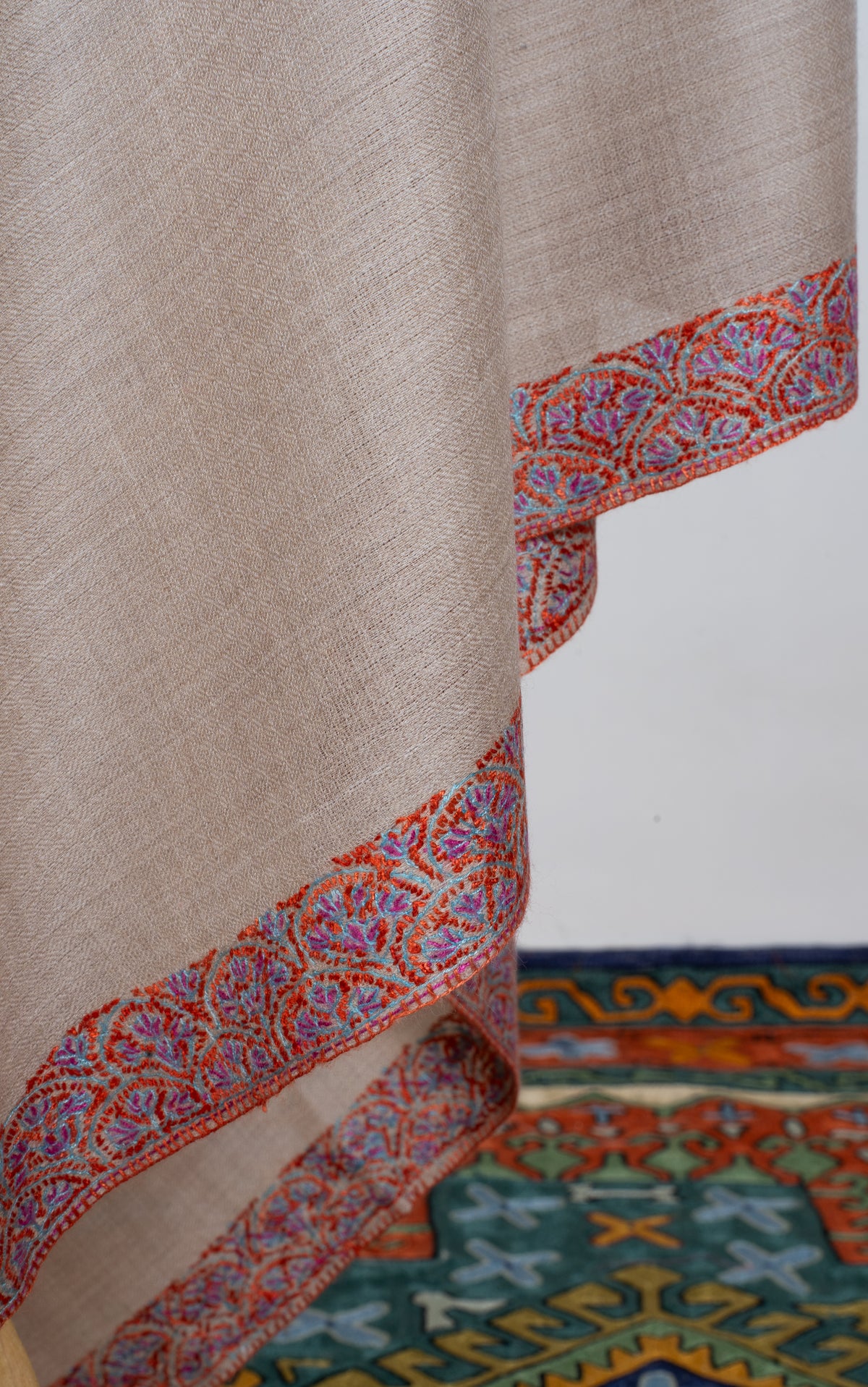Detail of the beige shawl’s hanging folds edged with a narrow multicoloured floral border