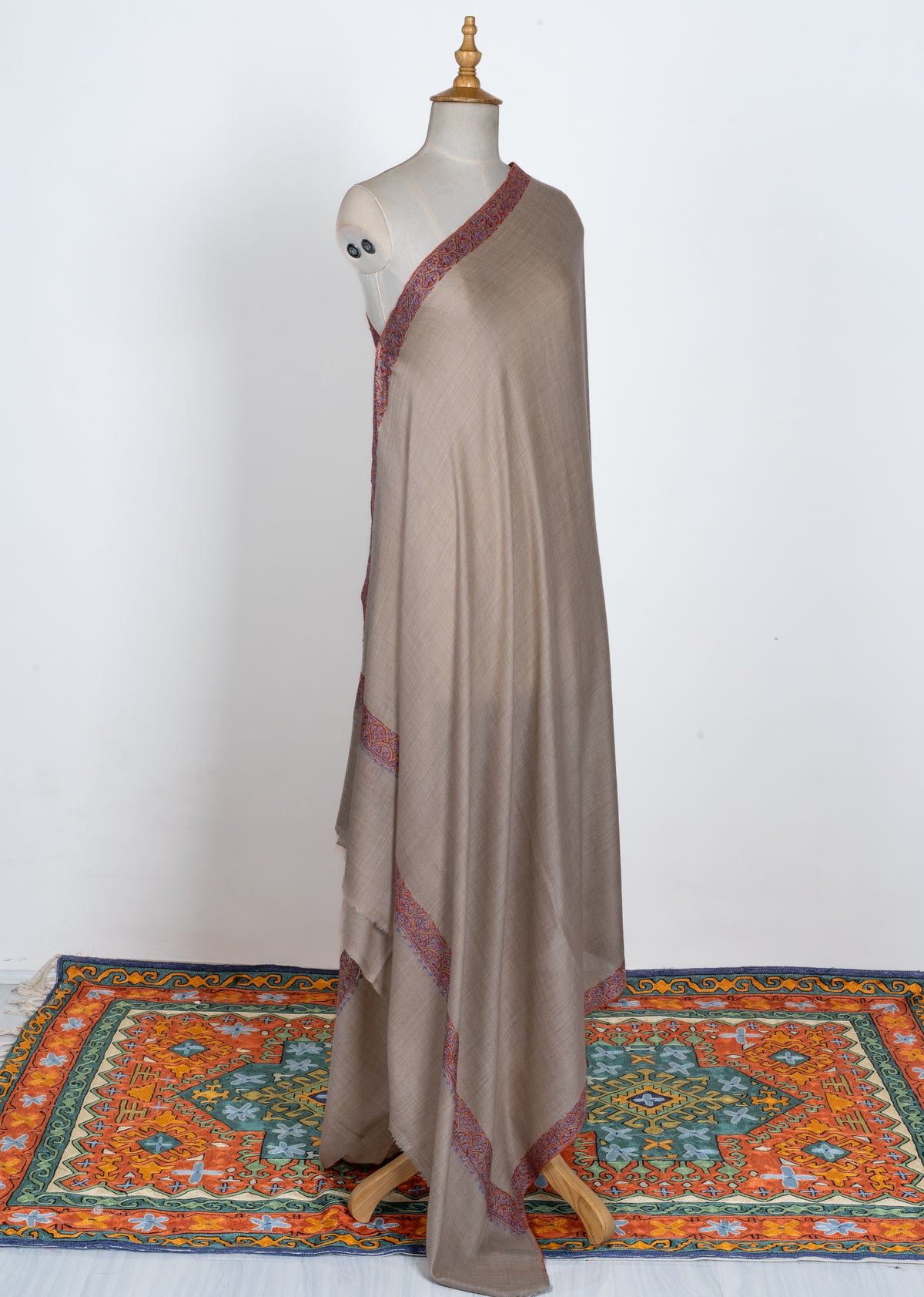 Full view of the beige shawl draped over a mannequin, showing its plain centre and multicoloured embroidered edges