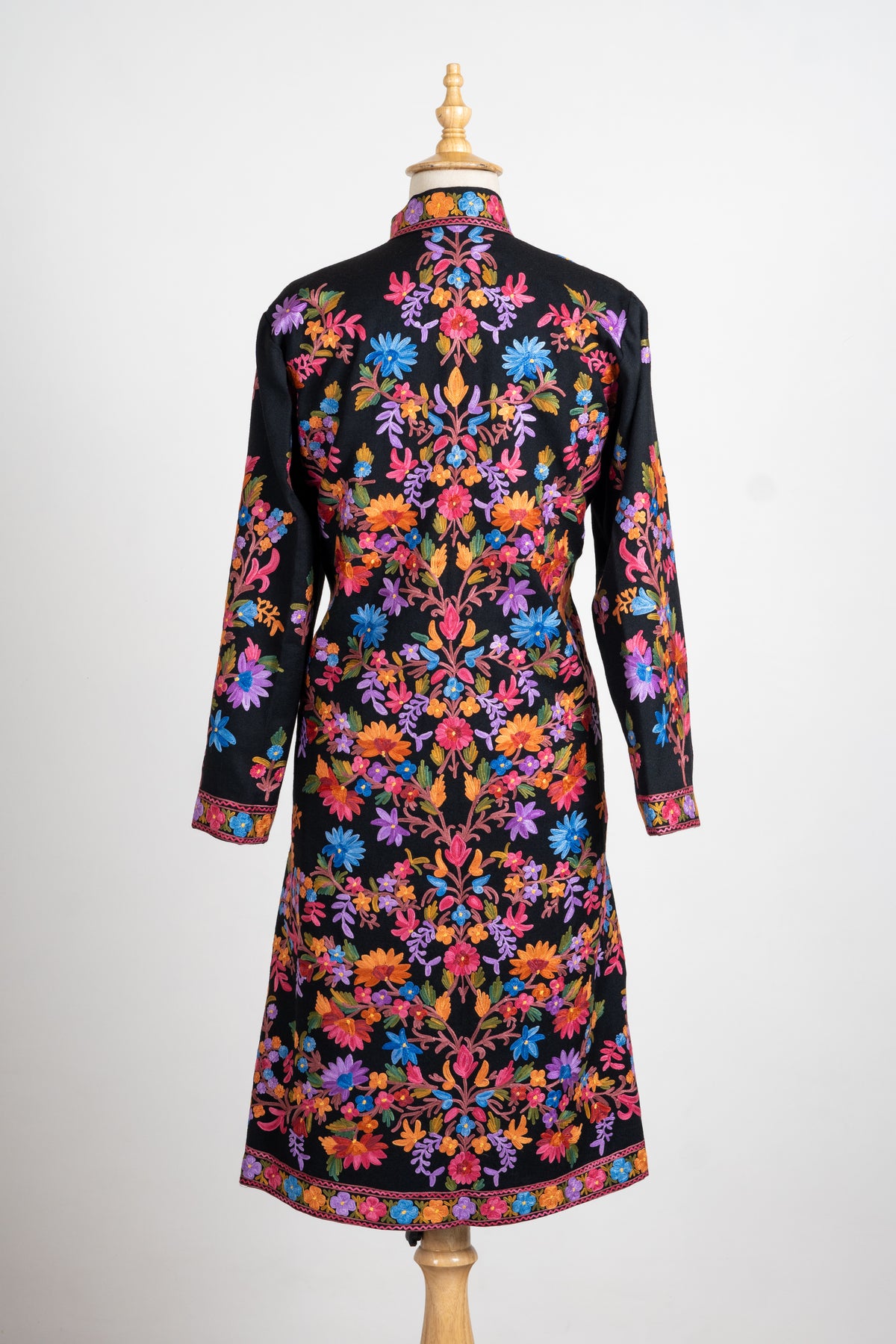 Back of the black long jacket covered with symmetrical pink, orange, blue and purple floral vines and bordered at the hem.