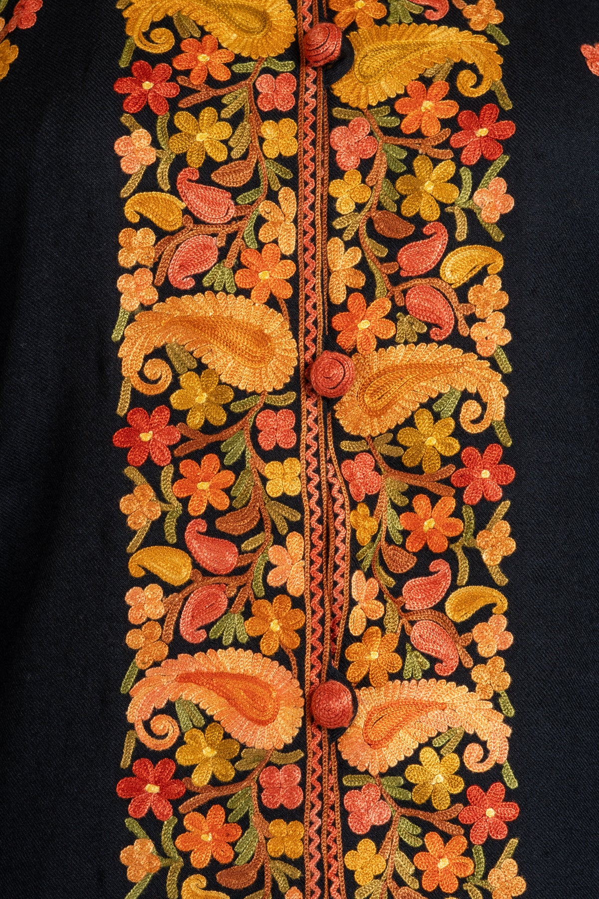 Close-up of gold and orange Aari paisleys and small flowers flanking covered buttons down the black jacket front