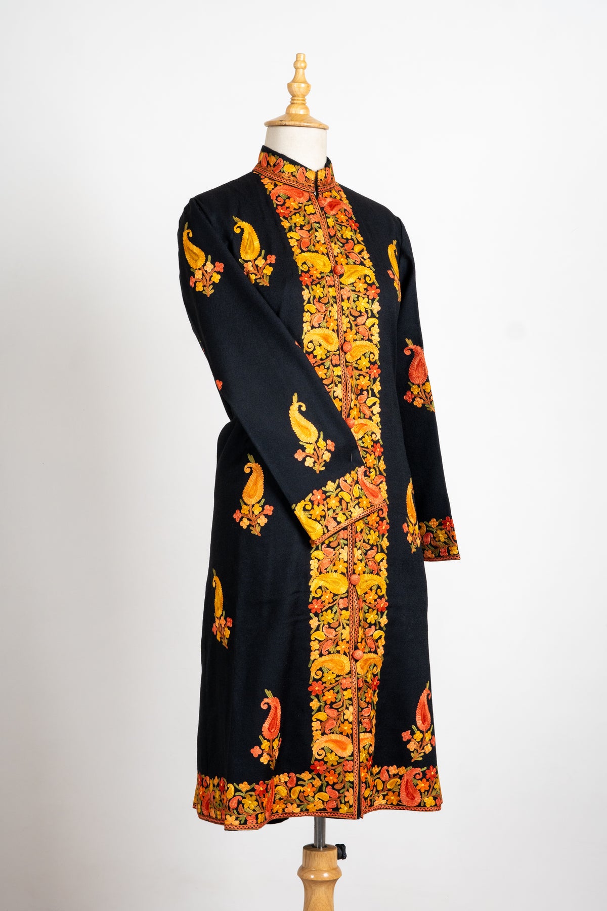 Angled full front of the black long jacket on a mannequin, with gold-orange paisley embroidery and one sleeve crossed