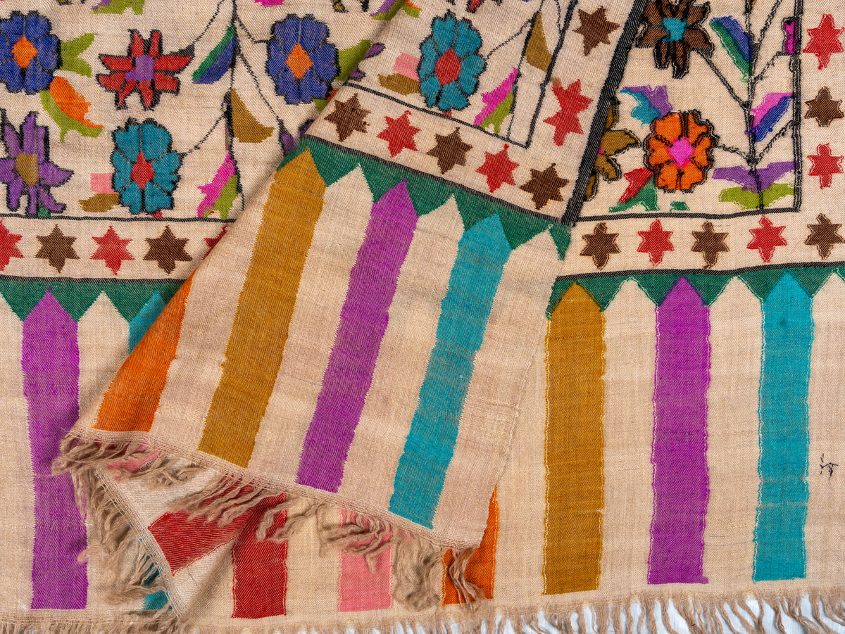 A close-up of a woven textile with a cream base, featuring vertical stripes in purple, orange, teal, and red, along with embroidered floral and star motifs.