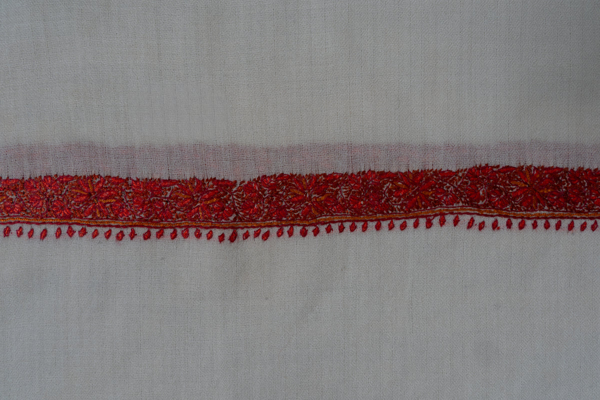 Close-up of a narrow crimson floral border and tiny red leaf motifs across the end of an ivory shawl