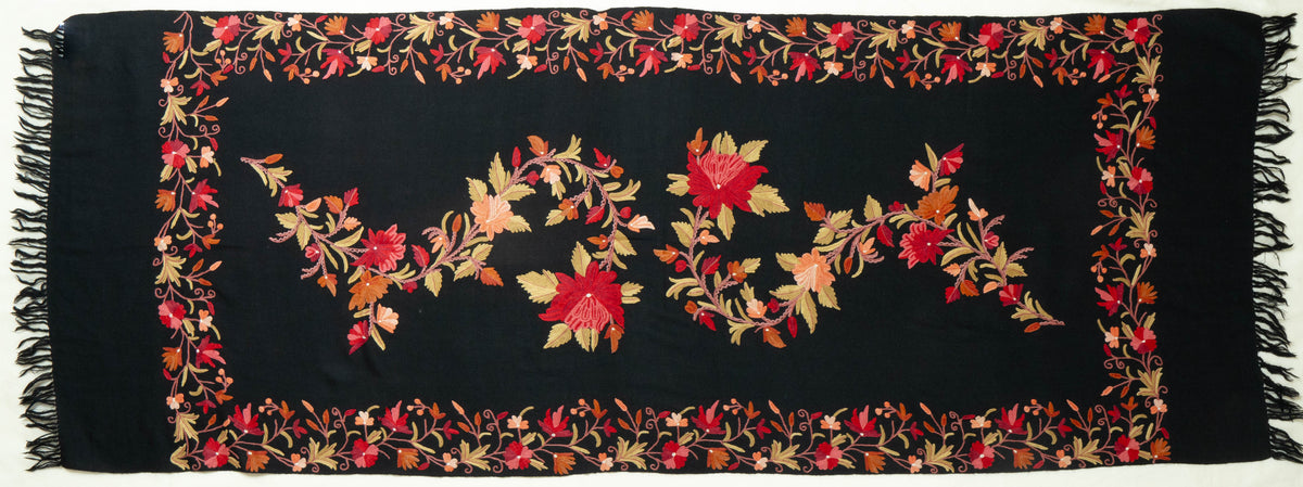 Black stole laid flat with a winding red and peach floral garland, rectangular embroidered border and fringed ends.