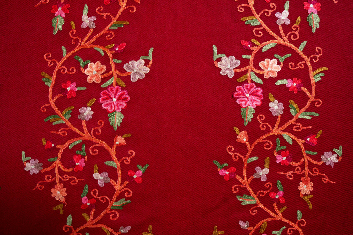 Flat detail of two curling Aari vines with pink, coral and pale lilac flowers and green leaves on crimson Merino wool
