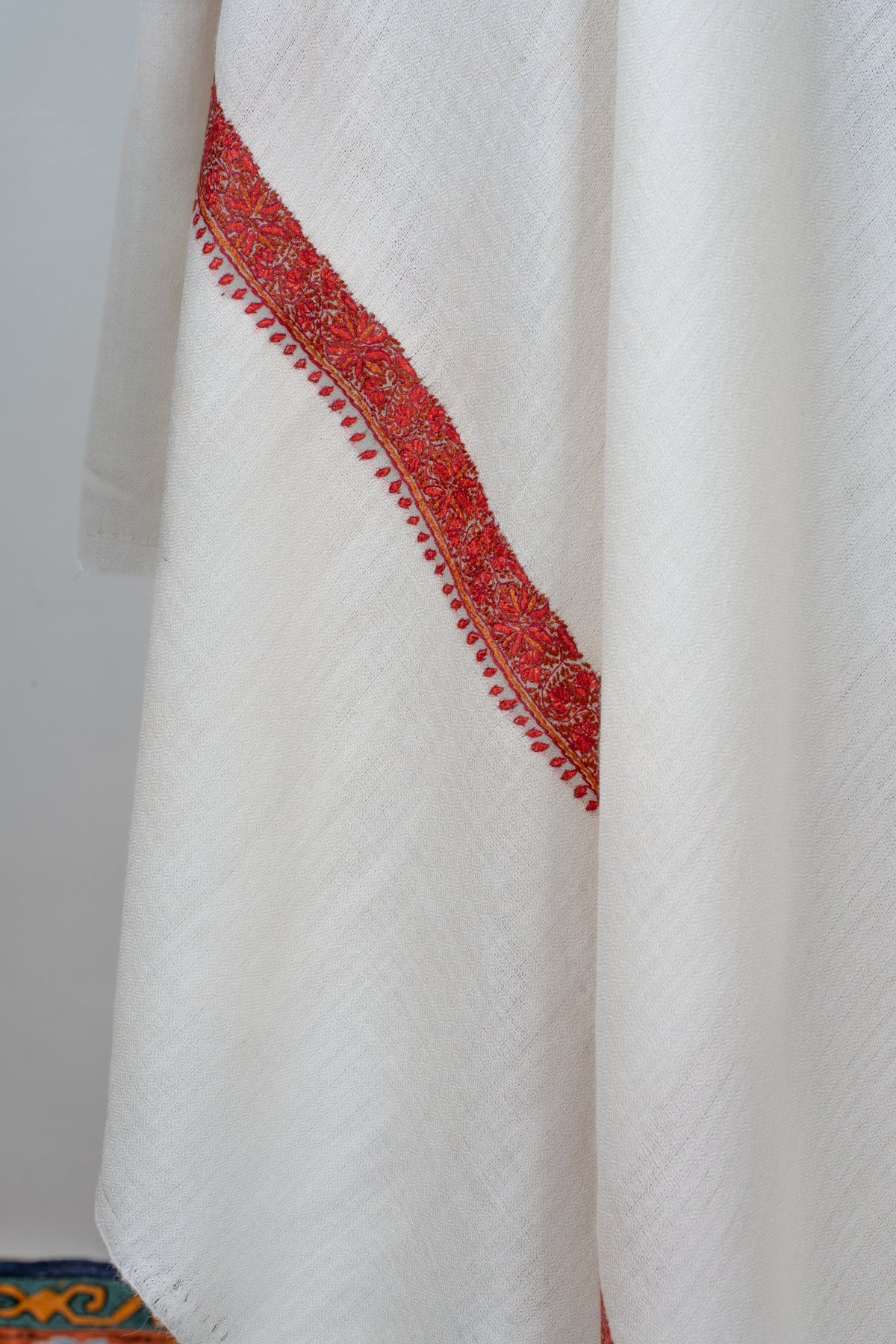 Hanging folds of an ivory shawl with a crimson floral border and a row of tiny red leaf motifs