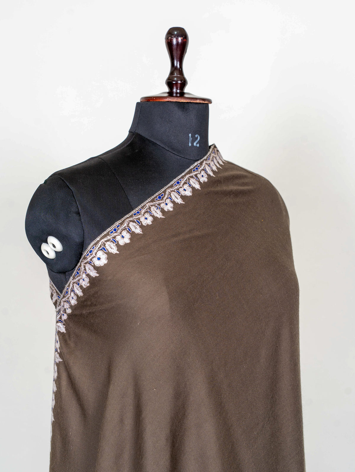 Angled shoulder view of the mocha-brown Pashmina shawl, with a narrow ivory floral border across the chest