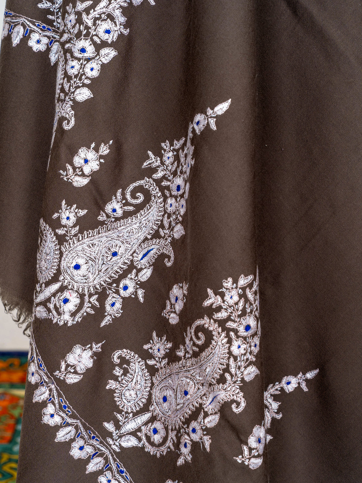 Detail of ivory floral and paisley Sozni embroidery along the draped end of the mocha-brown Pashmina shawl