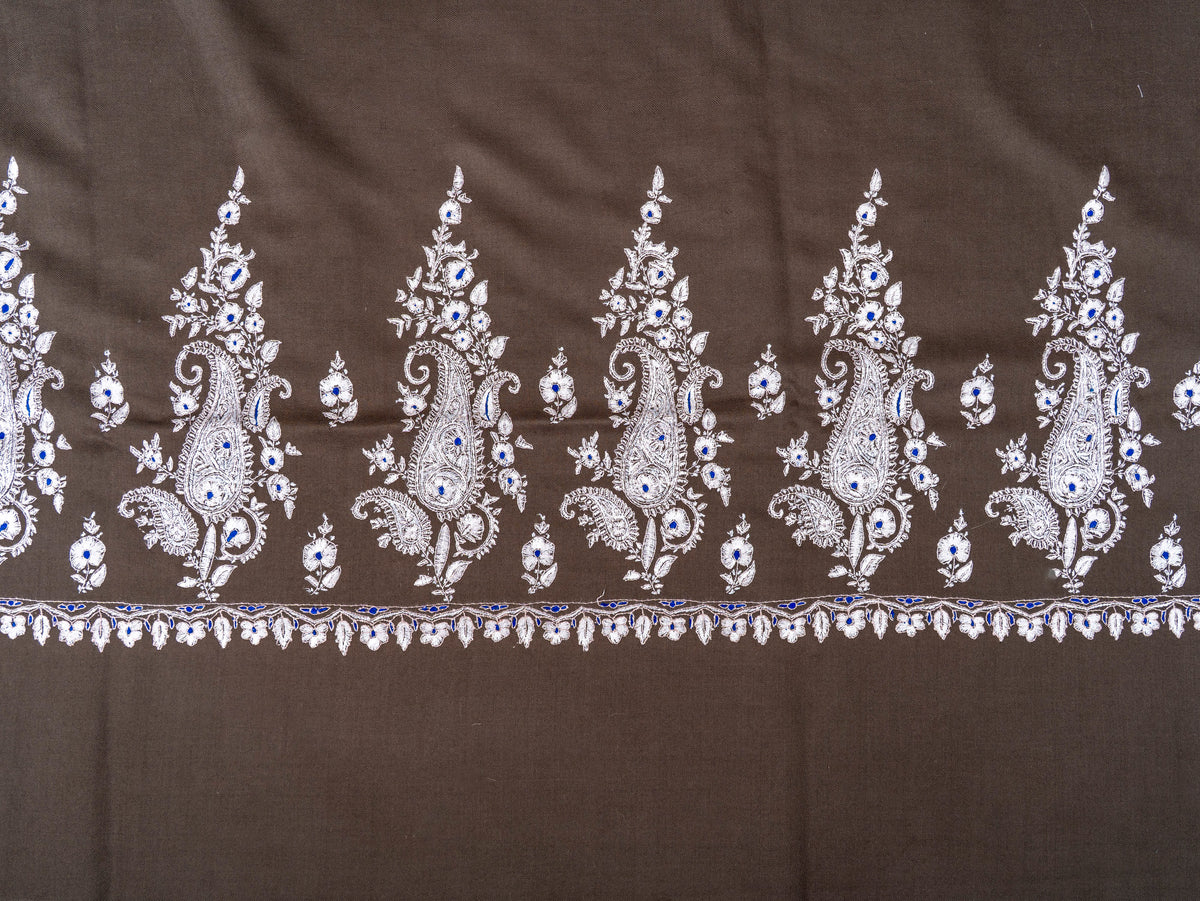 Close-up of repeating ivory Sozni paisley sprays and small flowers across the mocha-brown shawl's end border