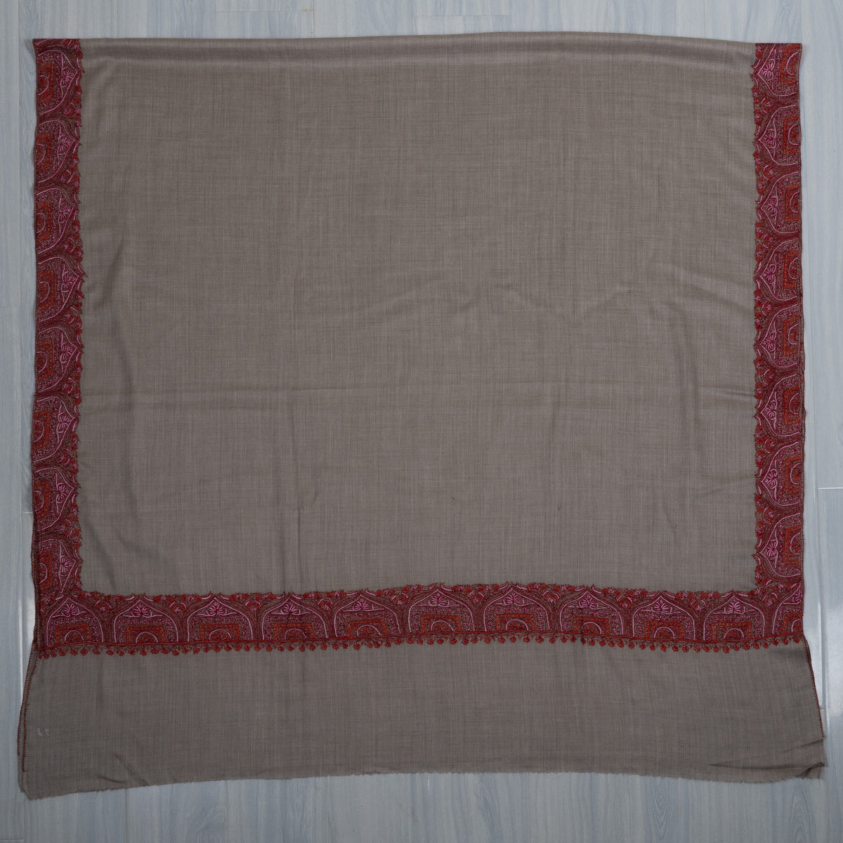 Ash-grey shawl spread flat, showing a plain centre framed by crimson embroidered borders.