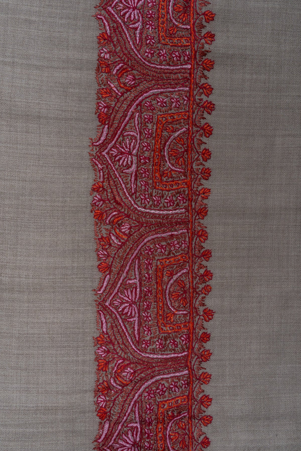 Close-up of the crimson and pink embroidered border against the shawl’s plain grey weave.