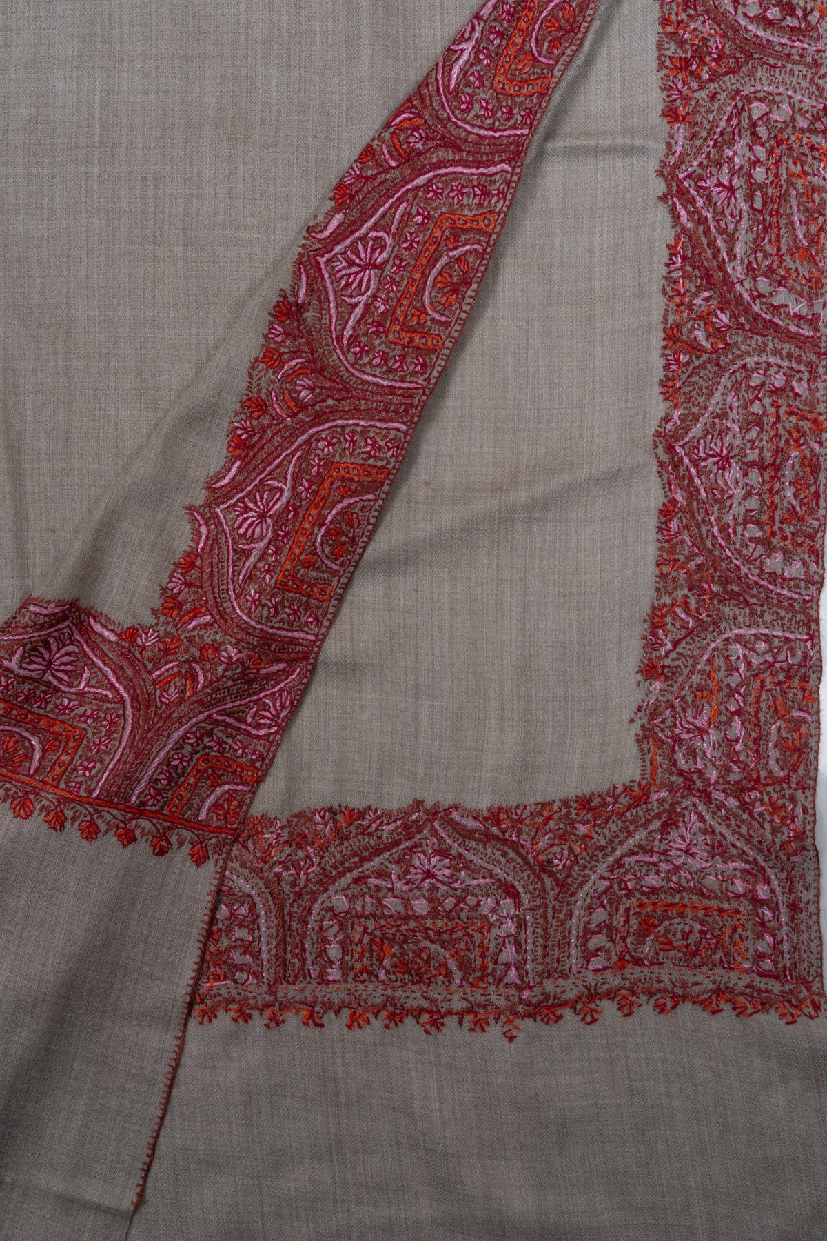 Folded grey shawl corner showing the front and reverse of its crimson and pink embroidered border.