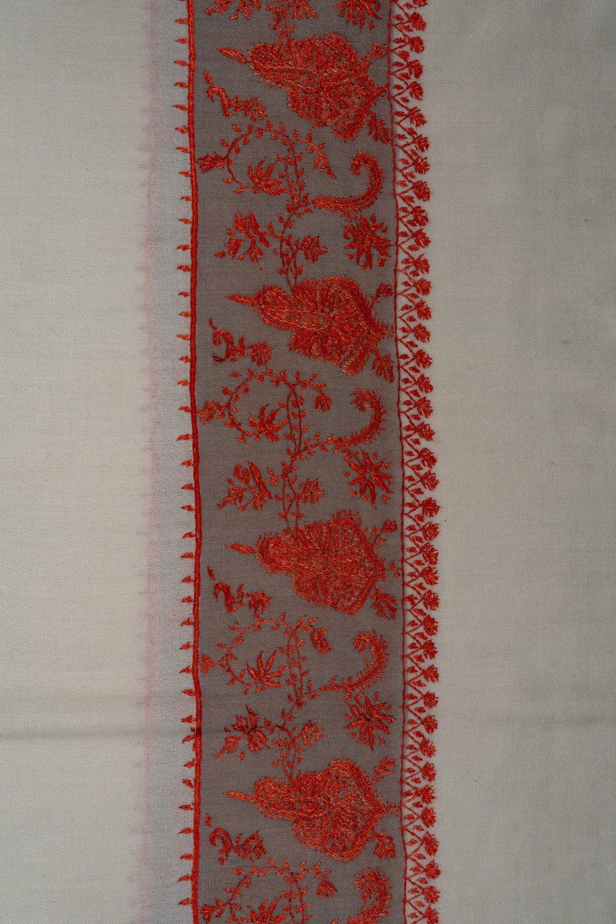Close-up of an ivory shawl border with red floral motifs and curling leafy vines on a pale grey band