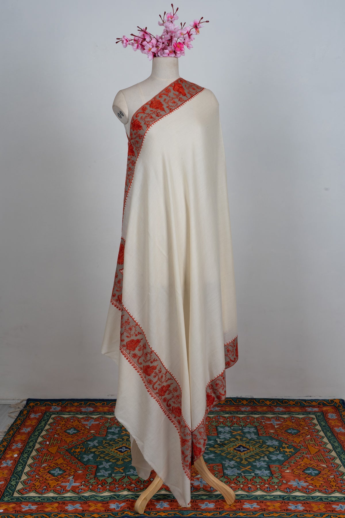 Full view of an ivory Merino wool shawl over one shoulder, with broad red floral borders and a plain body