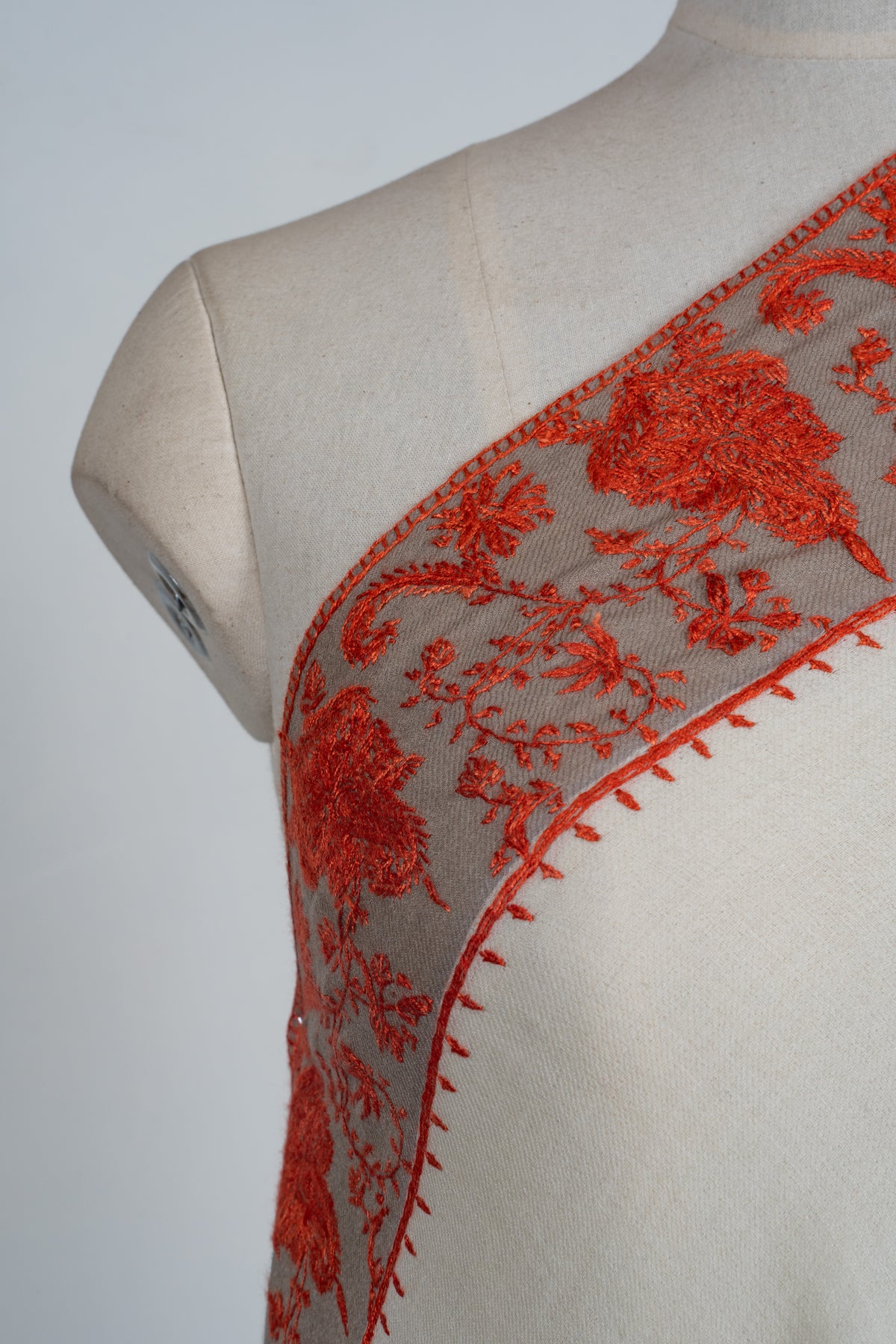 Close-up of an ivory shawl shoulder edge with red Sozni flowers and leafy vines on a pale grey border