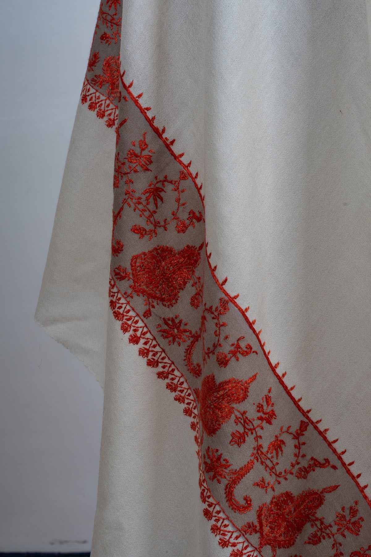 Draped ivory shawl edge with a broad red Sozni floral border and fine pointed stitching along its inner edge