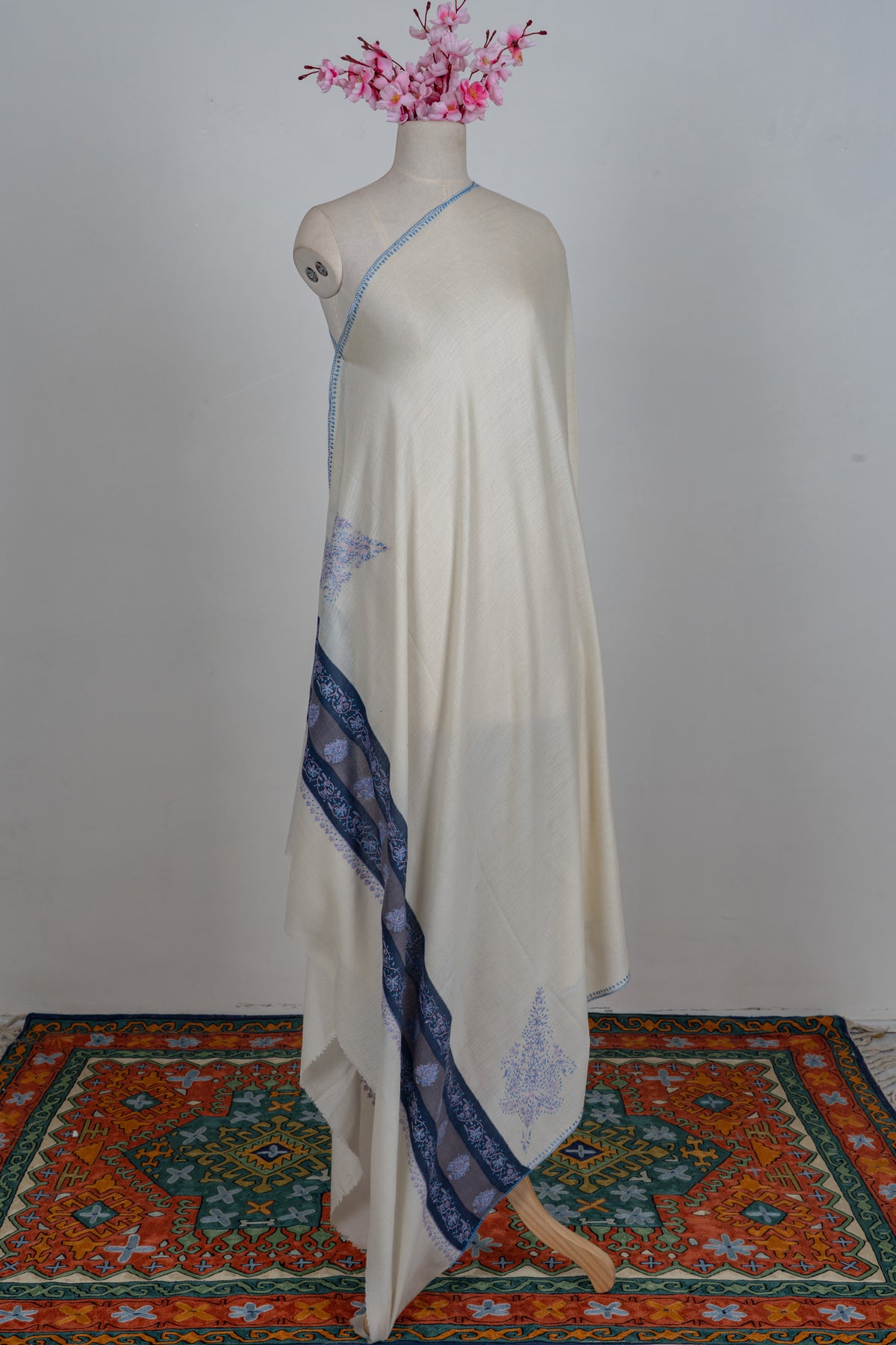Full view of the ivory Merino wool shawl draped on a mannequin with blue Sozni borders and corner motifs