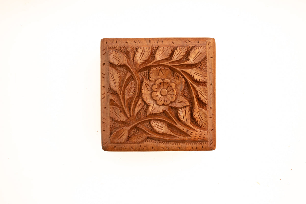 Overhead view of the walnut box lid carved with a central flower, curling stems and pointed leaves