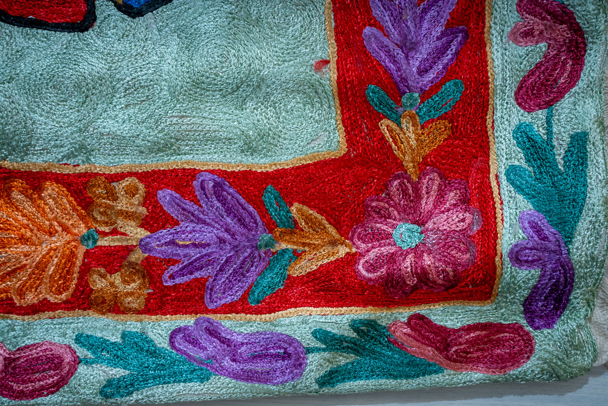 Corner close-up of the prayer mat's red floral border and pale green edge with purple and pink paisley motifs