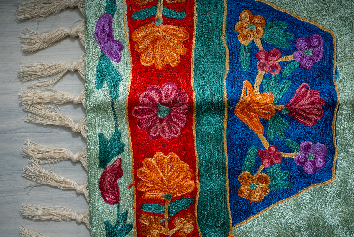 End detail of the prayer mat with a blue floral panel, red flower border and knotted cream tassels