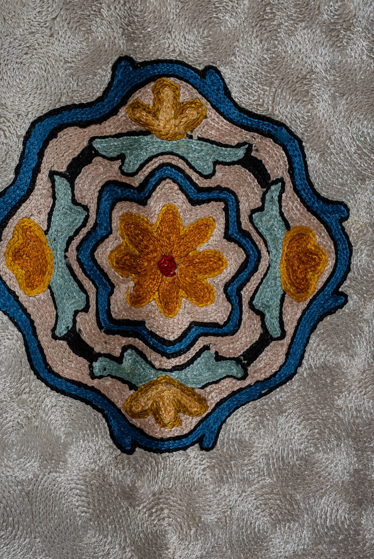 Close-up of a gold flower inside a blue and pink scalloped medallion on the textured ivory prayer mat