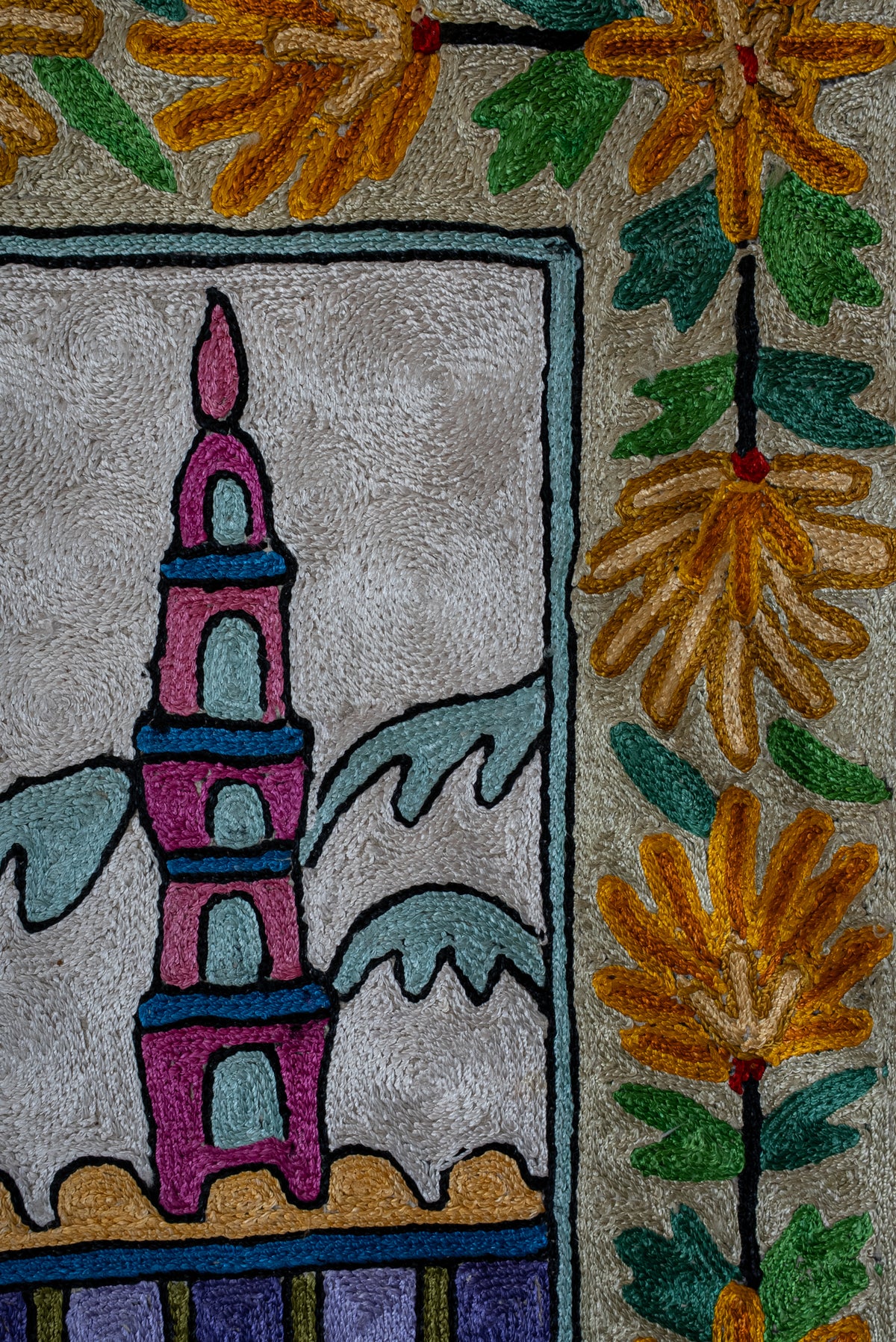 Pink minaret beside pale blue mountains and a yellow floral border with green leaves on the prayer mat