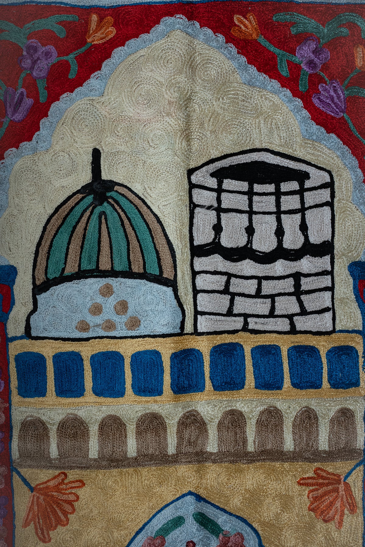 Close-up of a teal dome and black-and-white Kaaba beneath a pale blue arch on the prayer mat