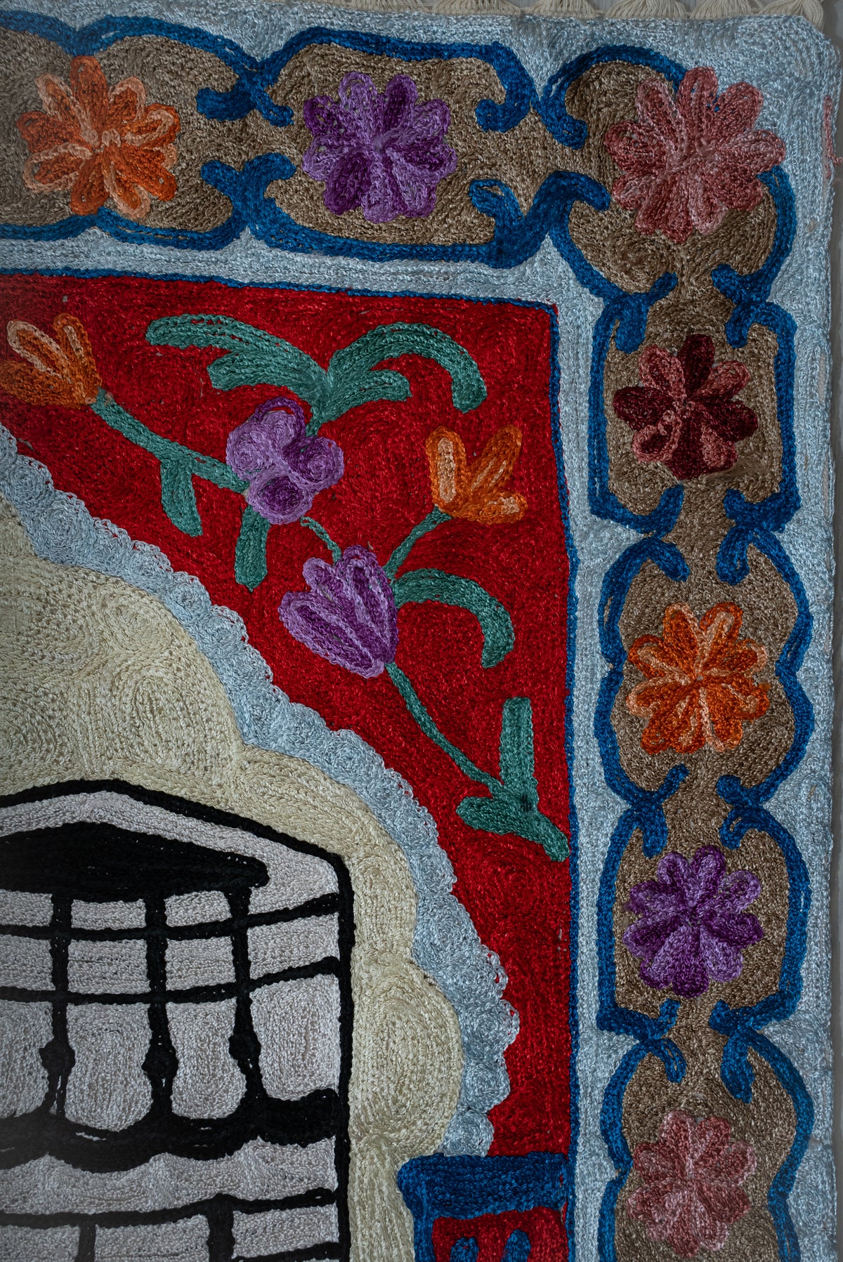 Upper corner of the prayer mat with purple and orange flowers, a red arch panel and a scalloped pale blue edge